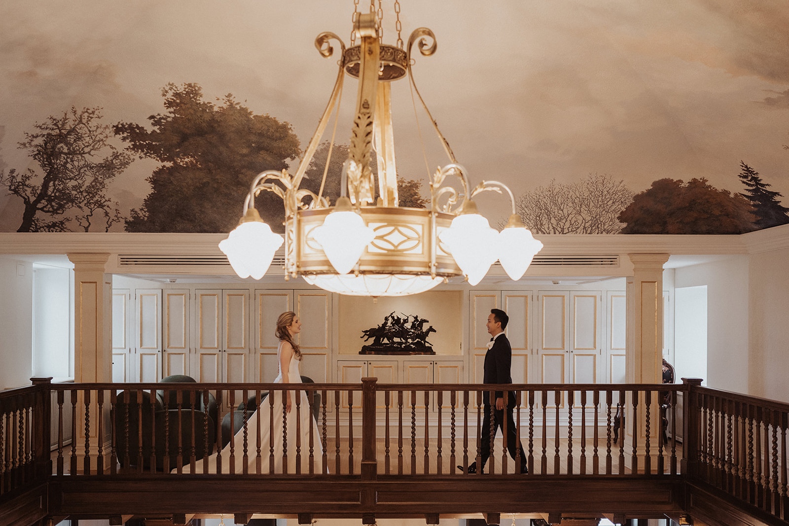 Couple under chandelier, wide shot with balanced symmetry.