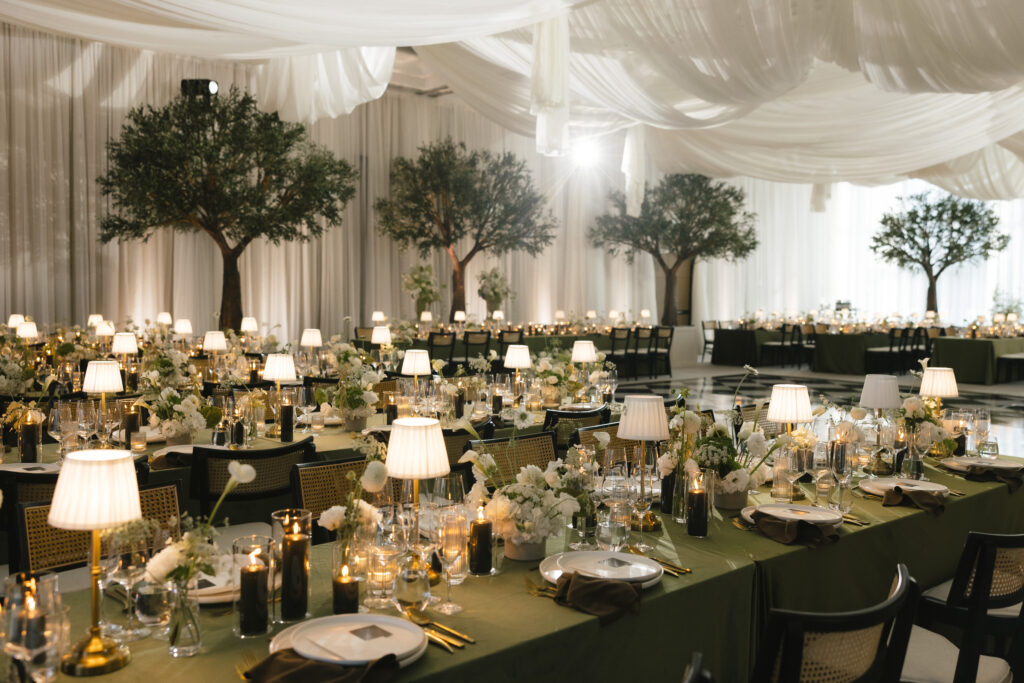 Styled by Total Events, elegant indoor wedding reception with long tables, green linens, candlelight, soft draping, and lush greenery creating a refined wedding reception atmosphere