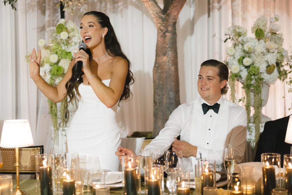 Bride giving a heartfelt wedding speech at the reception while seated NHL goaltender groom listens, surrounded by candlelit table decor and floral arrangements in Four Seasons Montreal