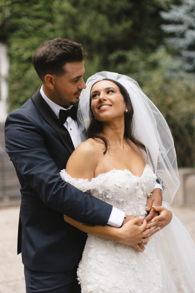 Bride and groom sharing a tender moment outdoors, with the bride in a delicate off-shoulder wedding gown from Dress Scoop and the groom in a classic tuxedo