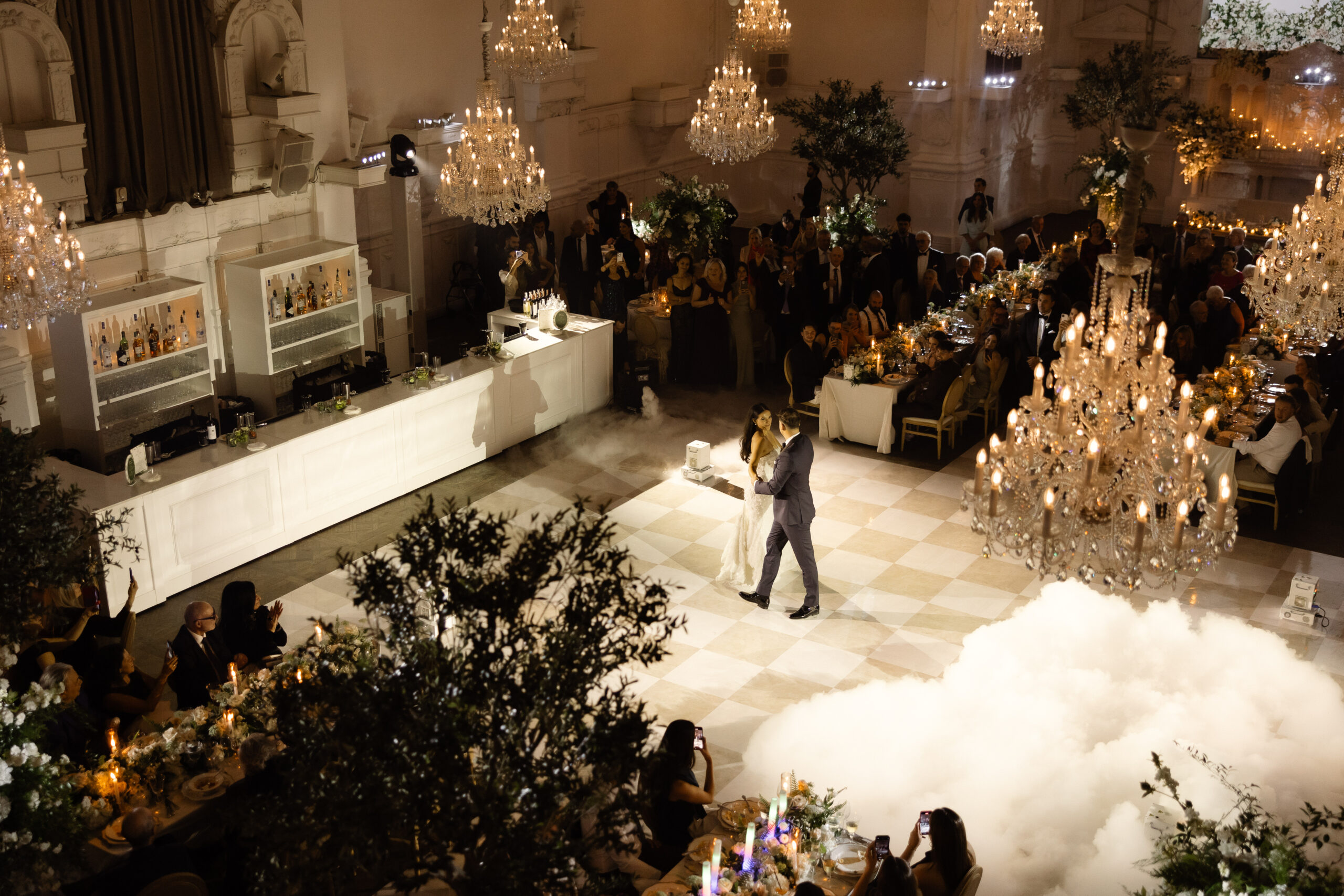 Olivia and Anthony share their first dance at Maison Principale, surrounded by guests and candlelit tables, with a dramatic chandelier overhead and a mist-filled dance floor.